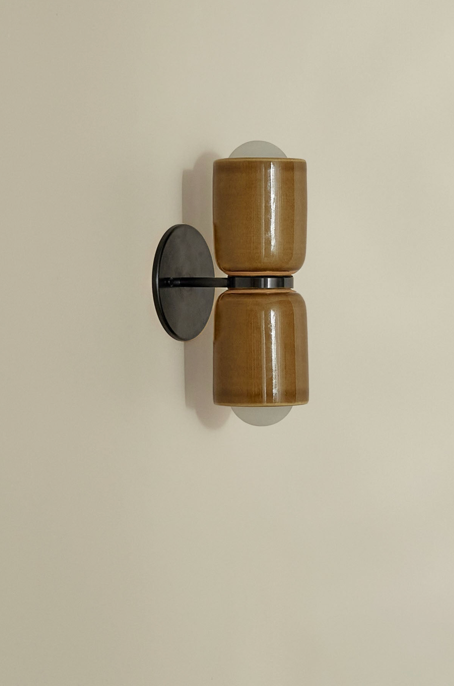 Wall-mounted light fixture with brown cylindrical shades on a beige wall.