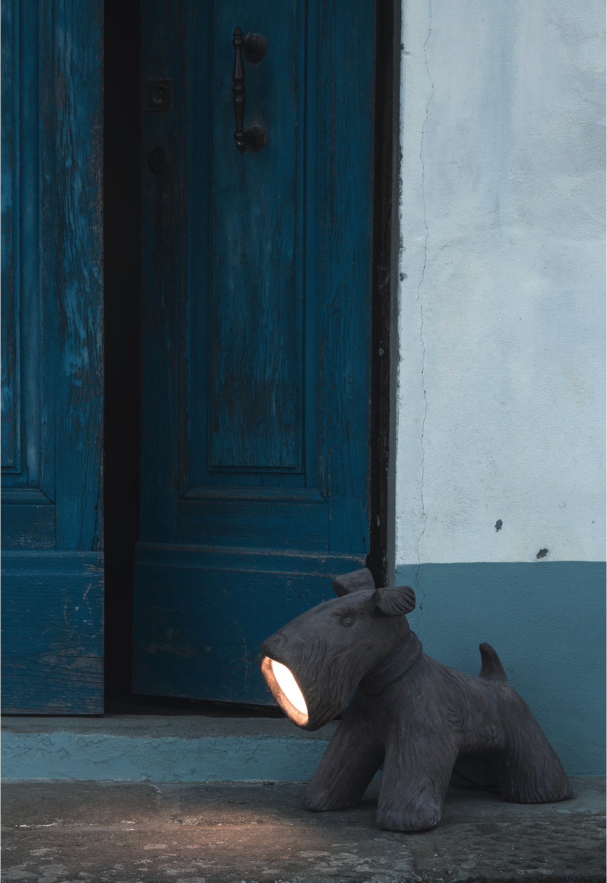 Dog-shaped lamp on a step in front of a blue door