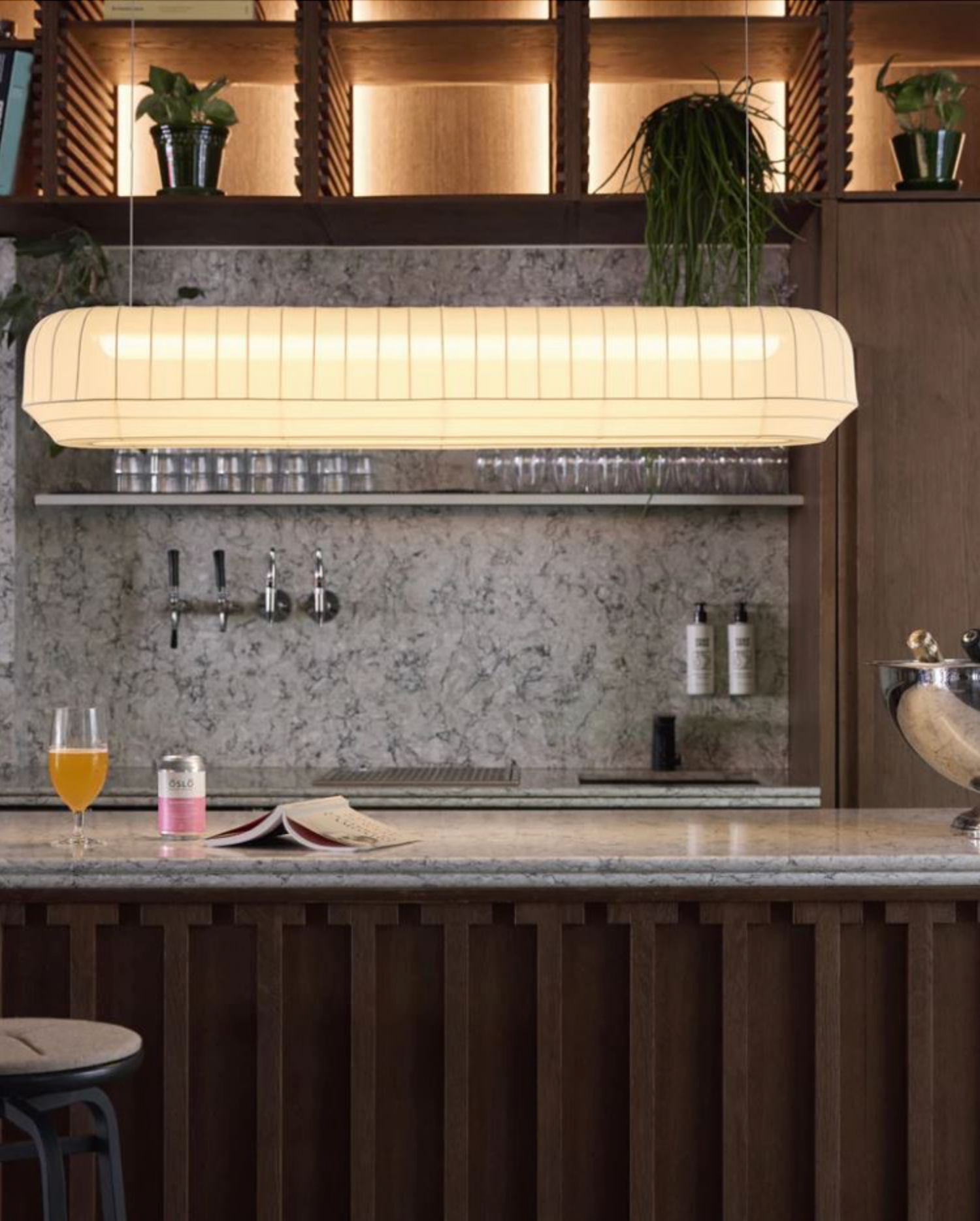 Modern bar counter with a linear pendant light, drinks, and decor.