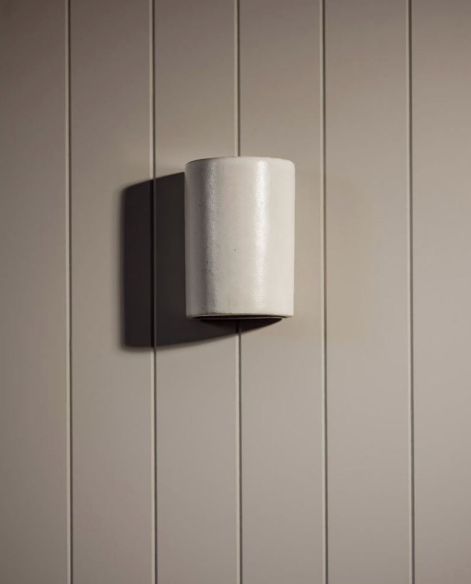 Ceramic cylindrical wall light fixture on a paneled wall