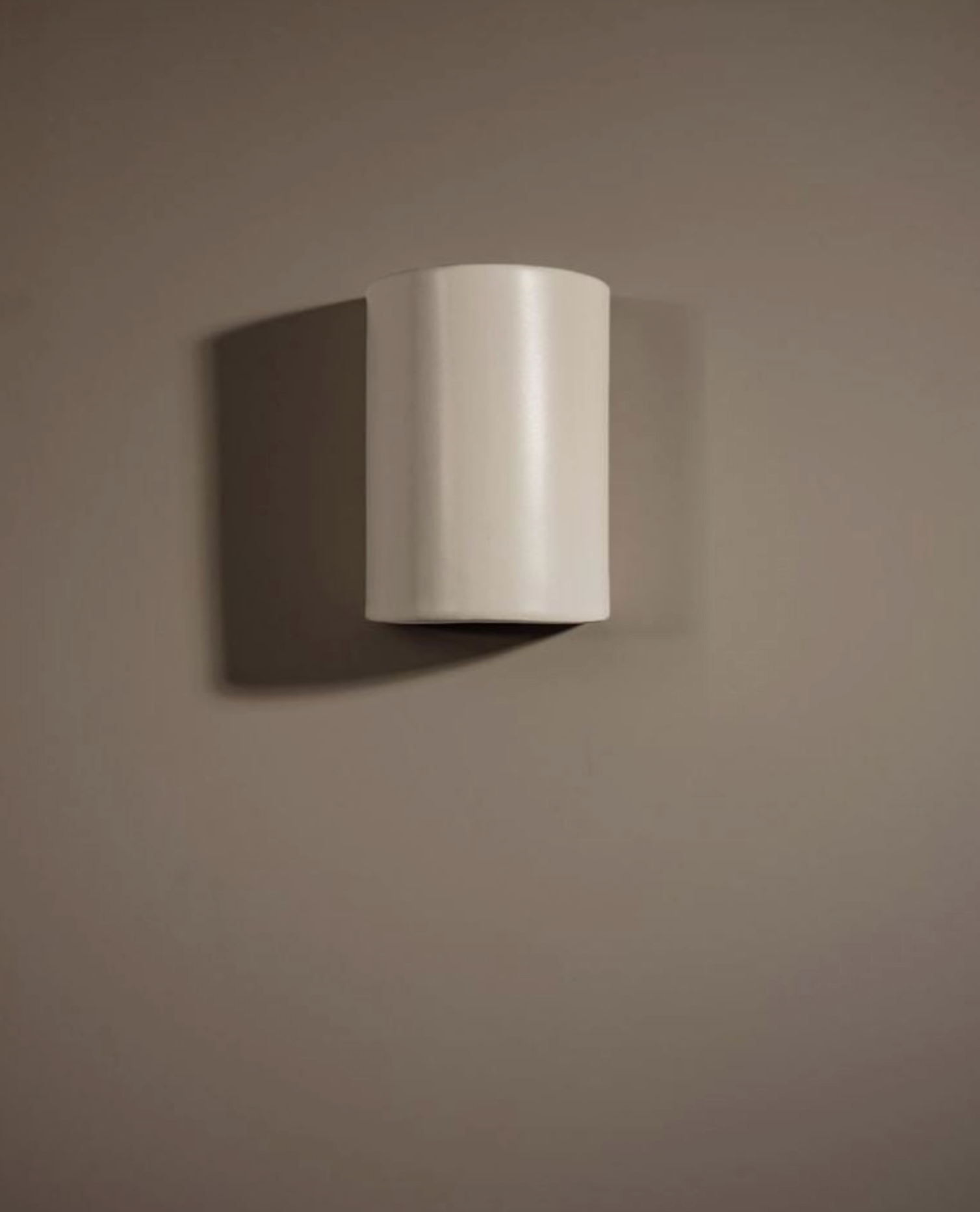White wall-mounted ceramic light fixture on a brown wall
