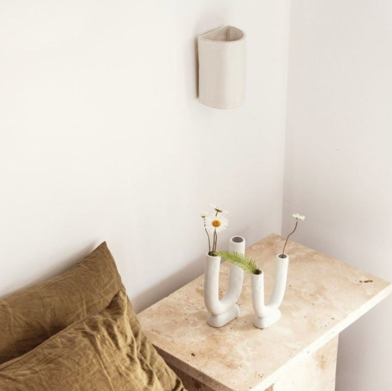 Nestled corner with a wooden side table, beige pillows, and decorative vases against a white wall.
