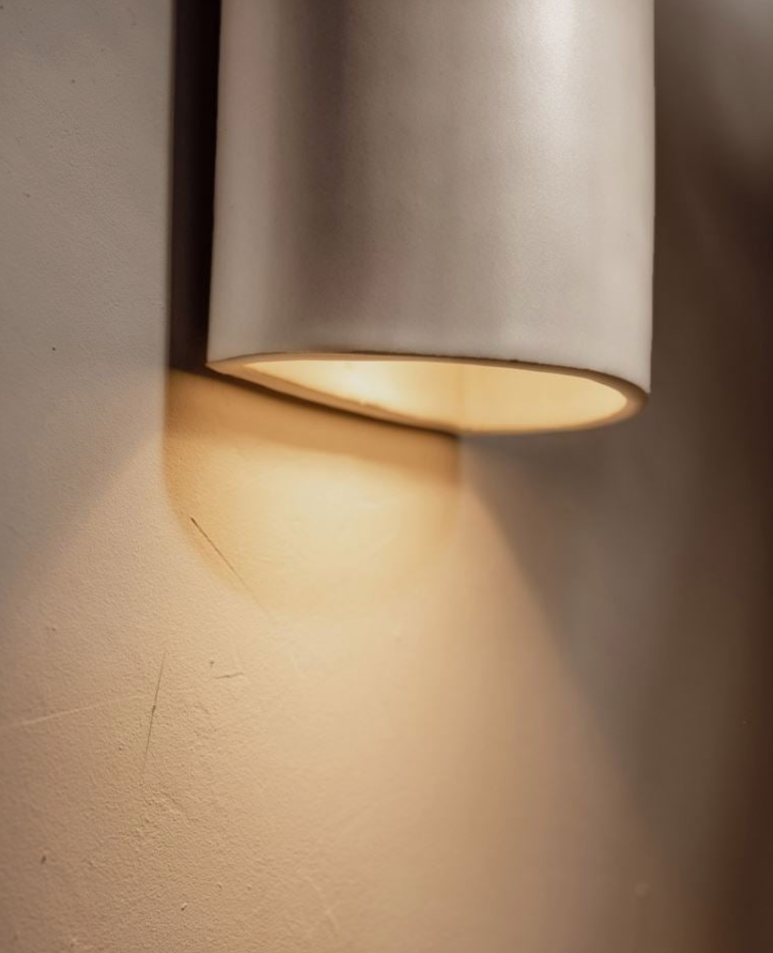 Wall-mounted cylindrical light fixture casting a warm glow on a textured wall.