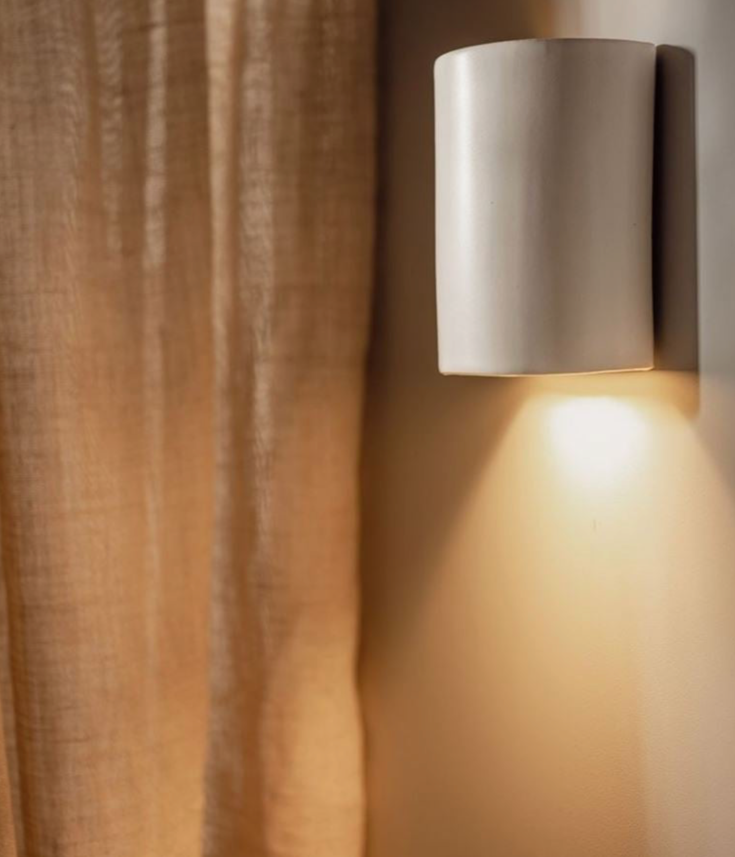 Wall-mounted outdoor light fixture casting a warm glow on a curtain.