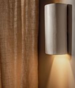 Cylindrical wall light fixture on a wall with a curtain in the background