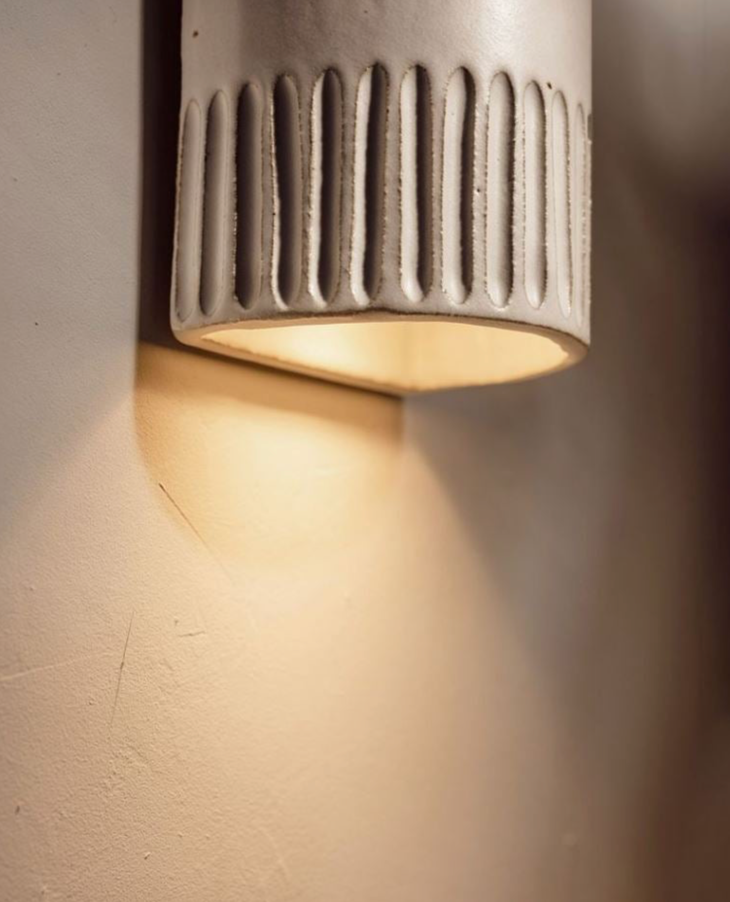 Ceramic wall light fixture emitting a warm glow on a textured wall.