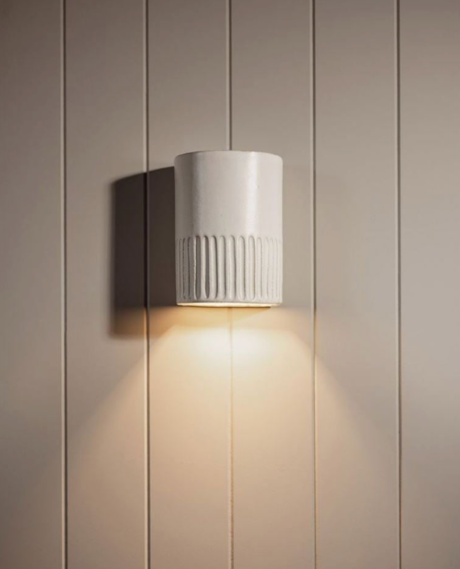 White wall-mounted light fixture on a beige paneled wall