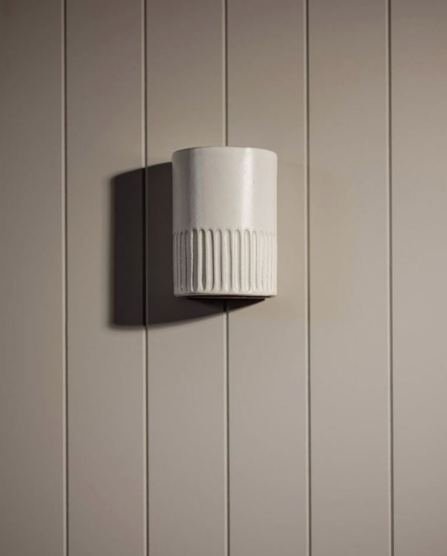 White cylindrical wall light fixture on a beige paneled wall