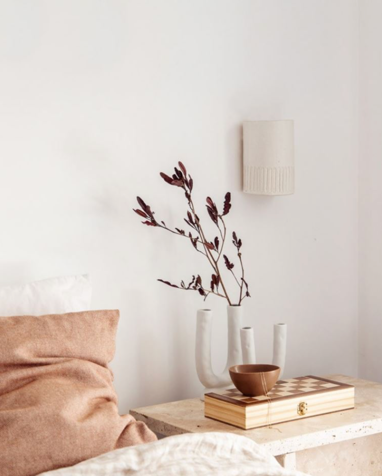 Decorative elements on a bedside table with a wall lamp and branches in a vase.