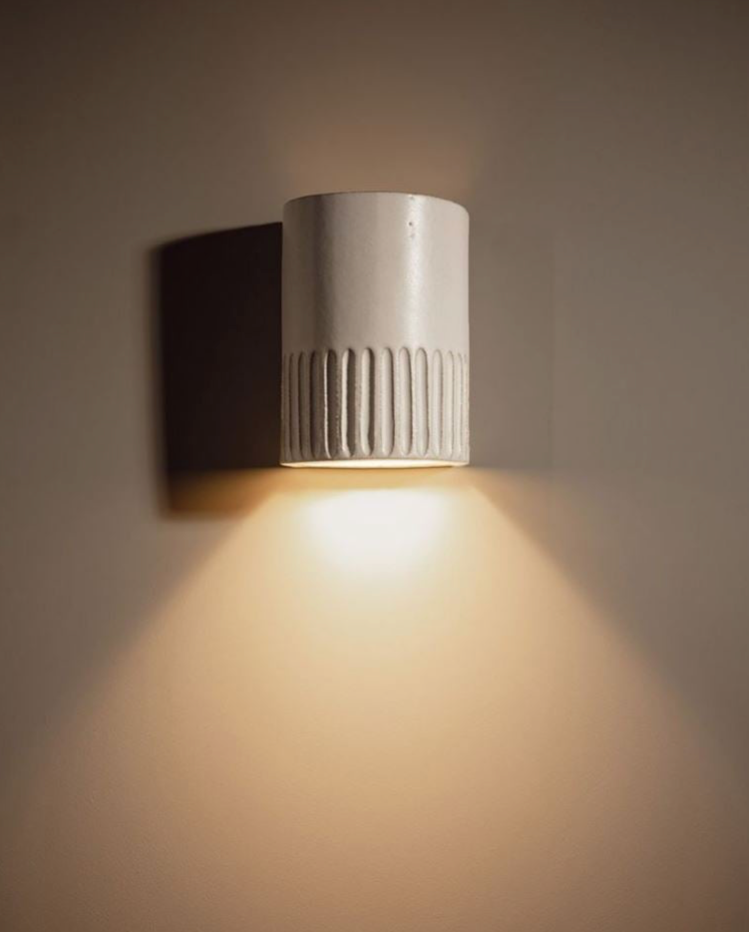 Ceramic interior wall light fixture casting a warm glow on a neutral background