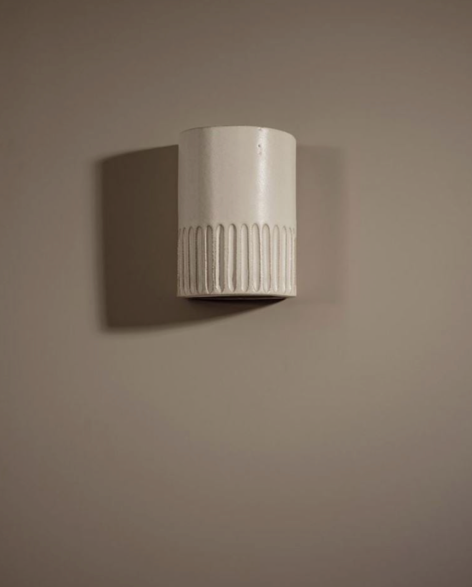 Cylindrical interior wall light fixture with textured surface on a beige wall.
