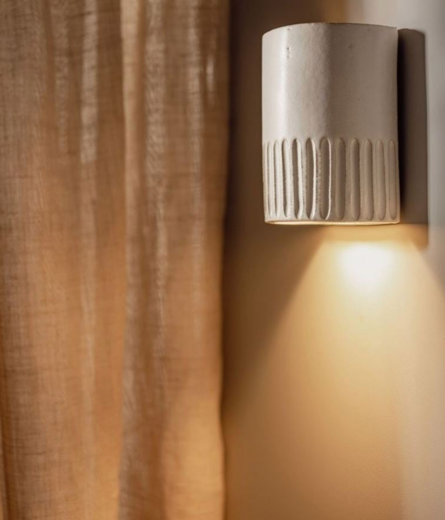 Ceramic wall light fixture on a textured wall with a curtain in the background