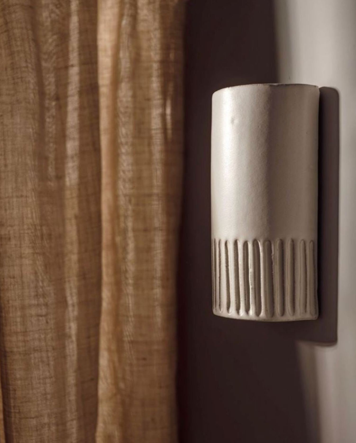 Metallic wall-mounted device with textured surface against a curtain background