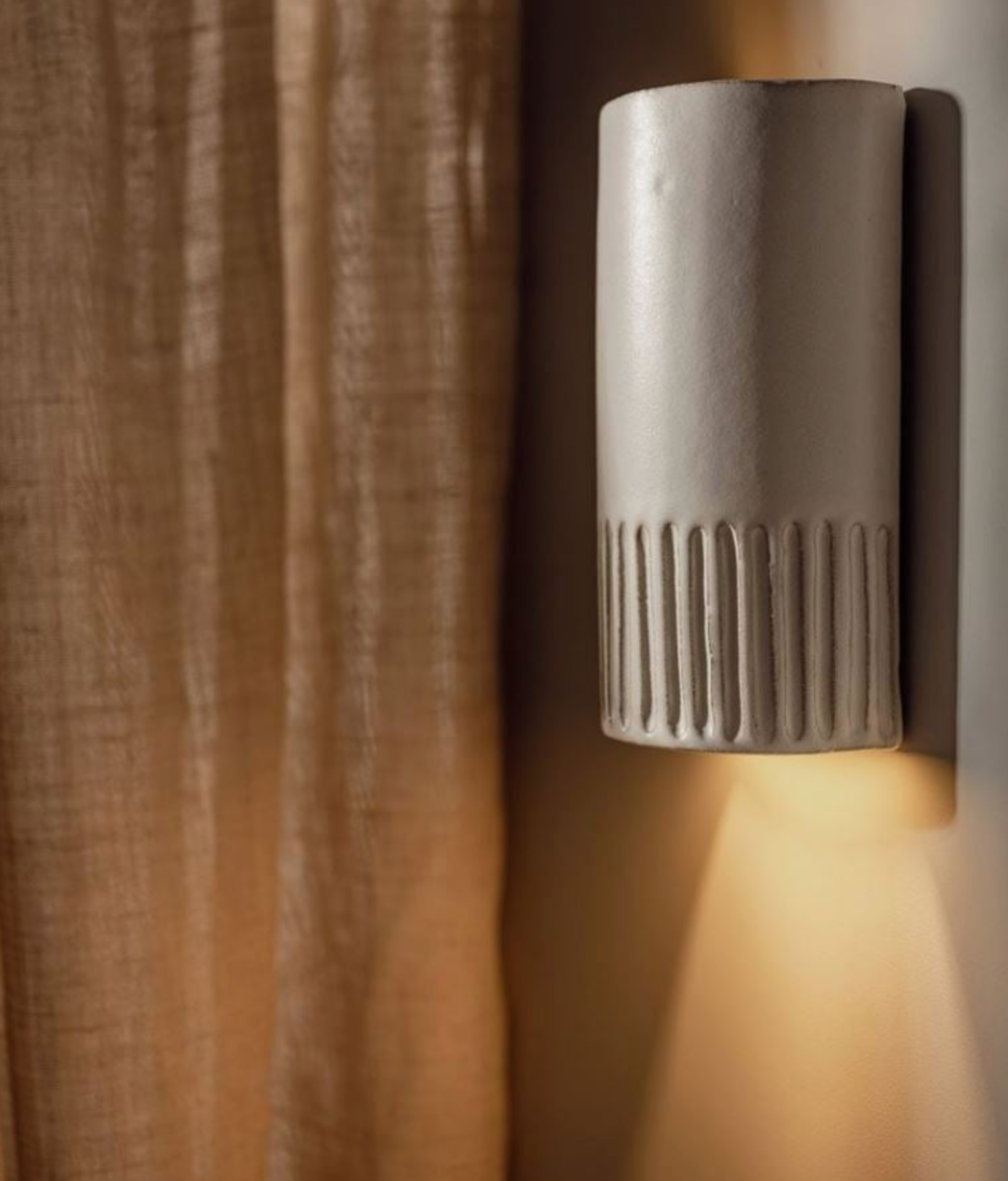 Ceramic textured interior wall sconce casting a warm glow on a textured wall.