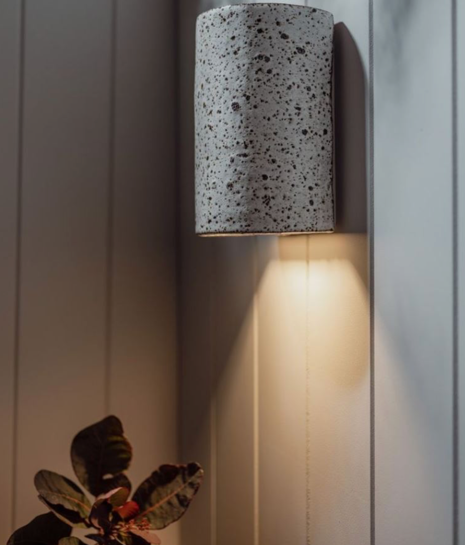 Cylindrical outdoor wall light fixture with speckle pattern on a panelled wall.