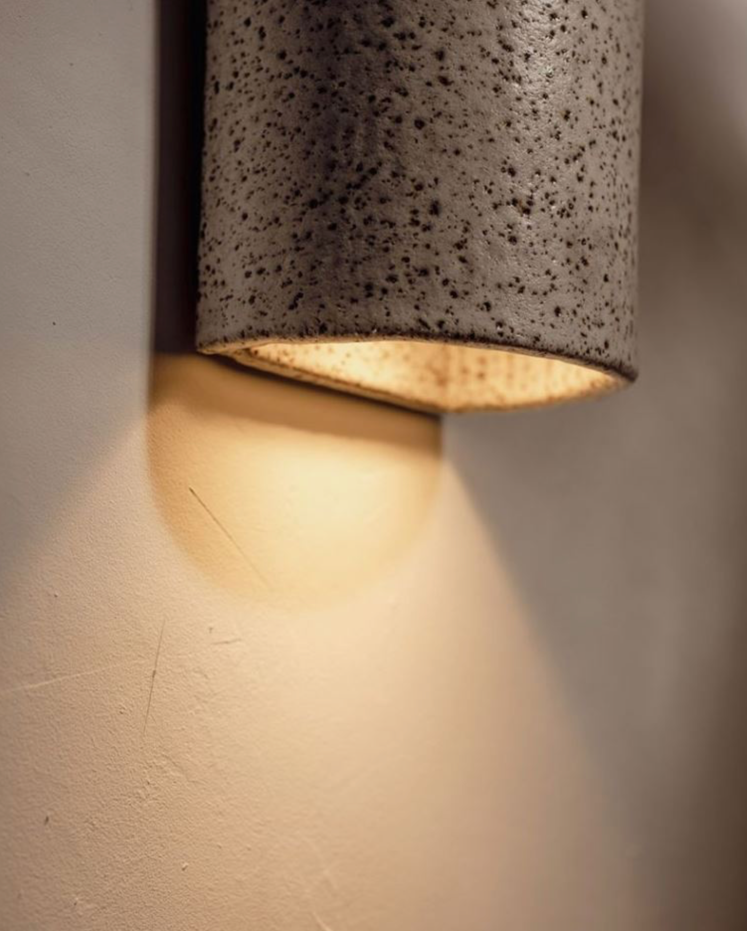 Cylindrical ceramic exterior wall light fixture on a neutral wall.