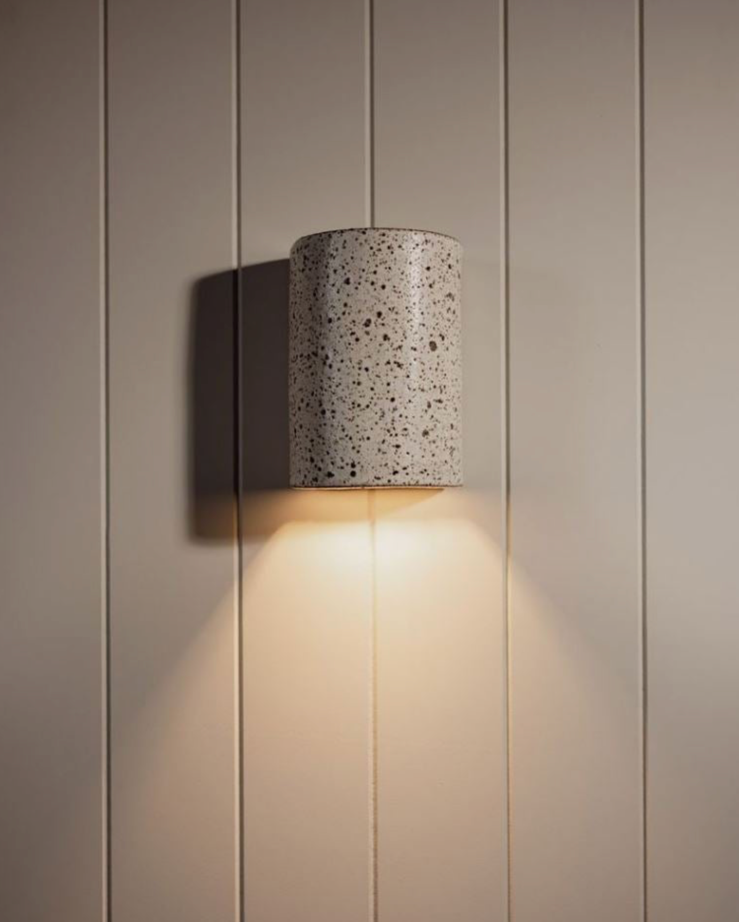 Wall-mounted lamp with speckled pattern casting light on a panel wall