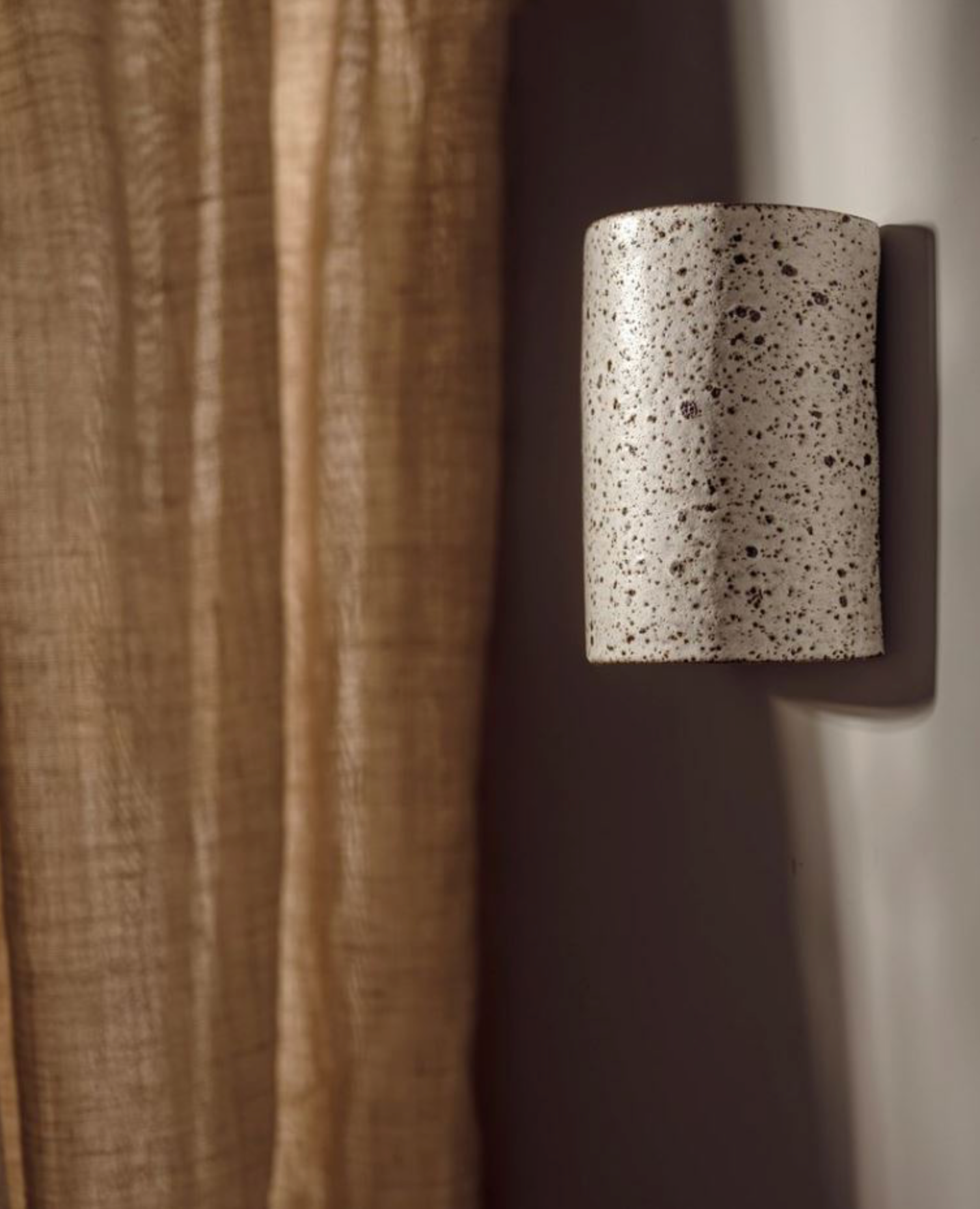 Speckled interior wall sconce mounted on a textured wall next to a curtain