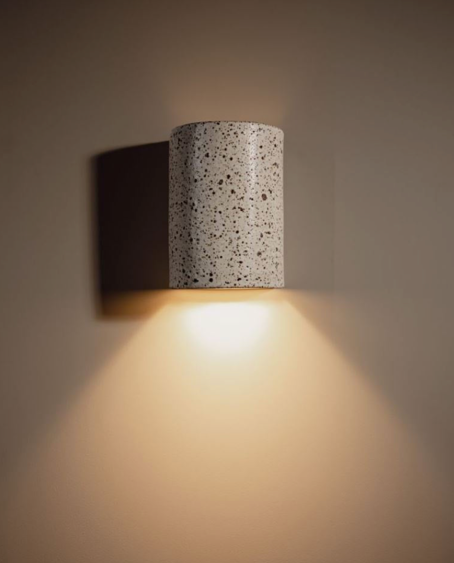 Cylindrical indoor wall light fixture with textured surface on a plain wall.
