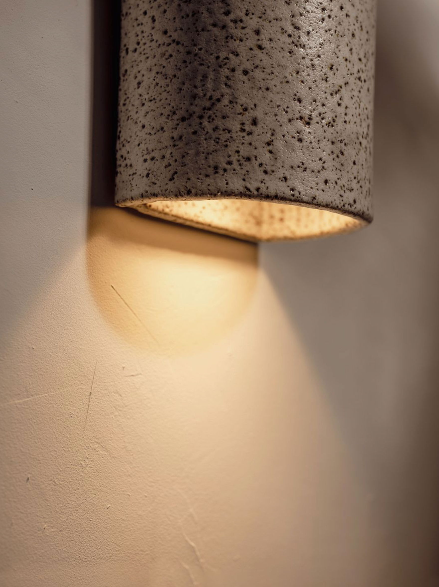 Cylindrical ceramic wall light fixture casting a warm glow on a neutral wall.