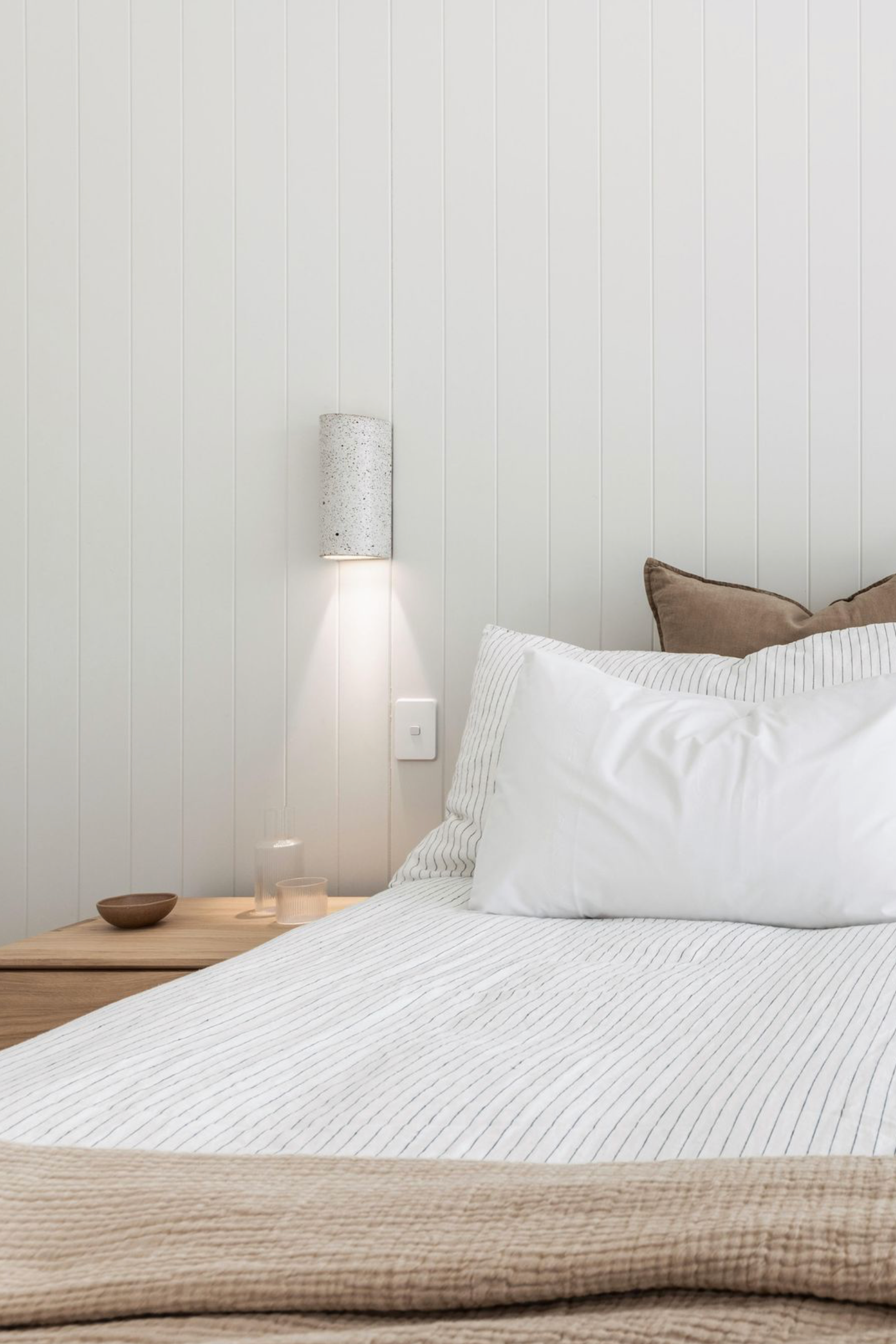 Neatly made bed with white bedding and pillows in a bedroom setting with a wall light.