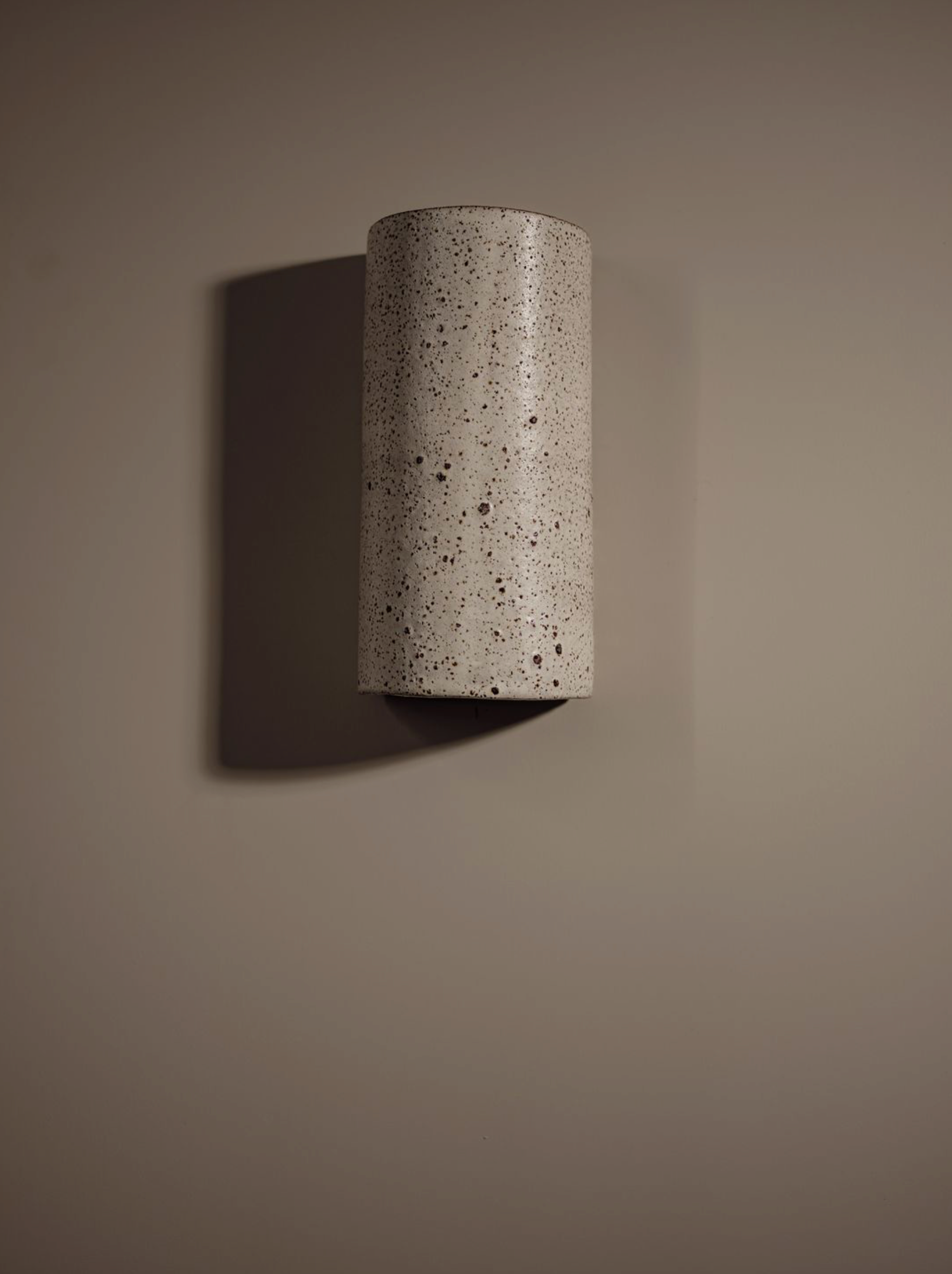 Cylindrical ceramic interior wall light fixture on a brown wall