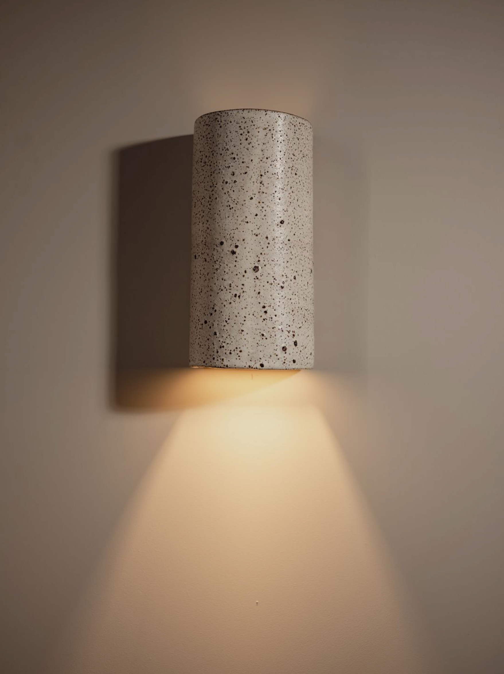 Ceramic wall light fixture casting a warm glow on a neutral background
