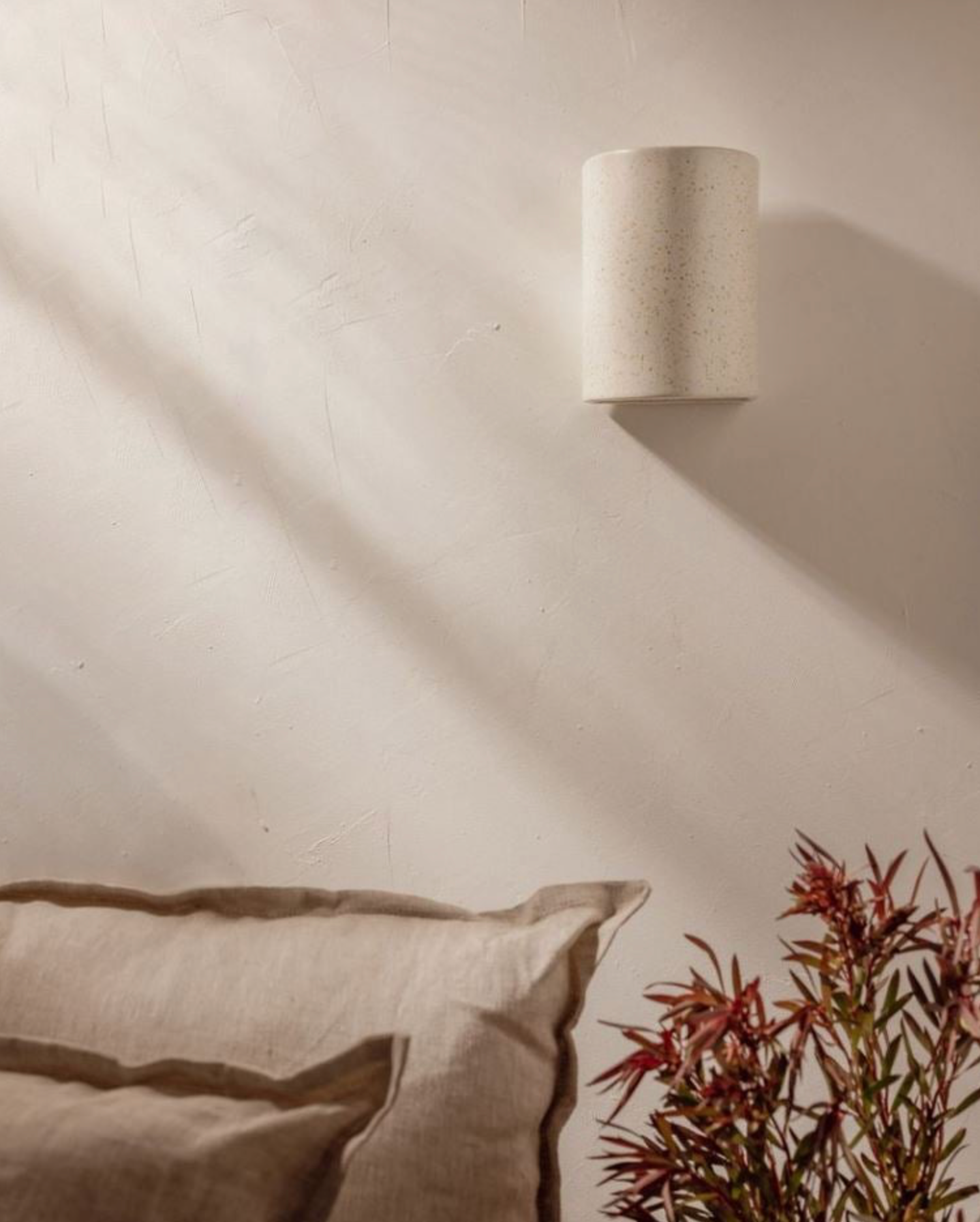 Ceramic wall sconce on a neutral wall with a pillow and plant in the foreground