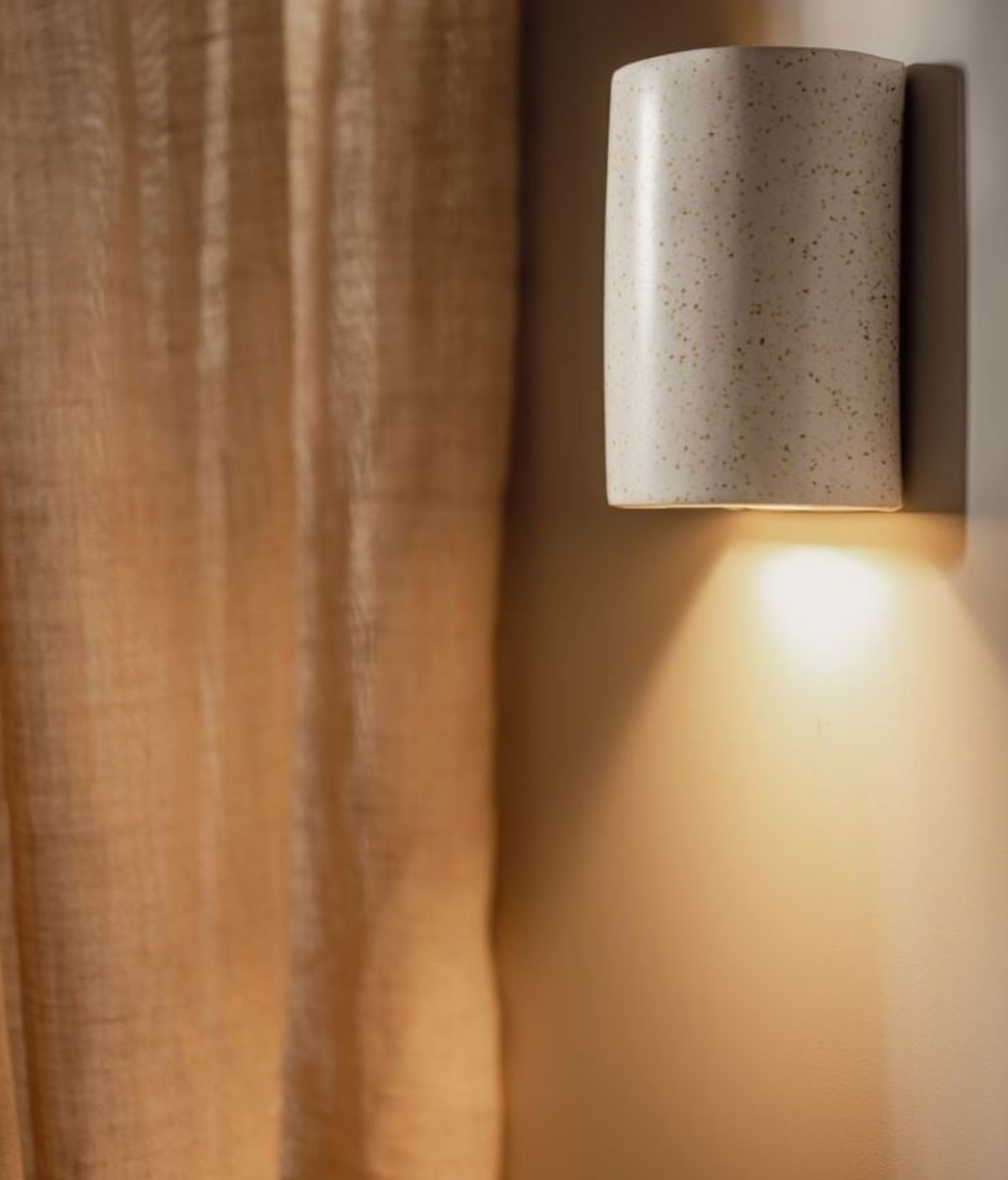Ceramic hand made wall light fixture casting a warm glow on a textured wall.