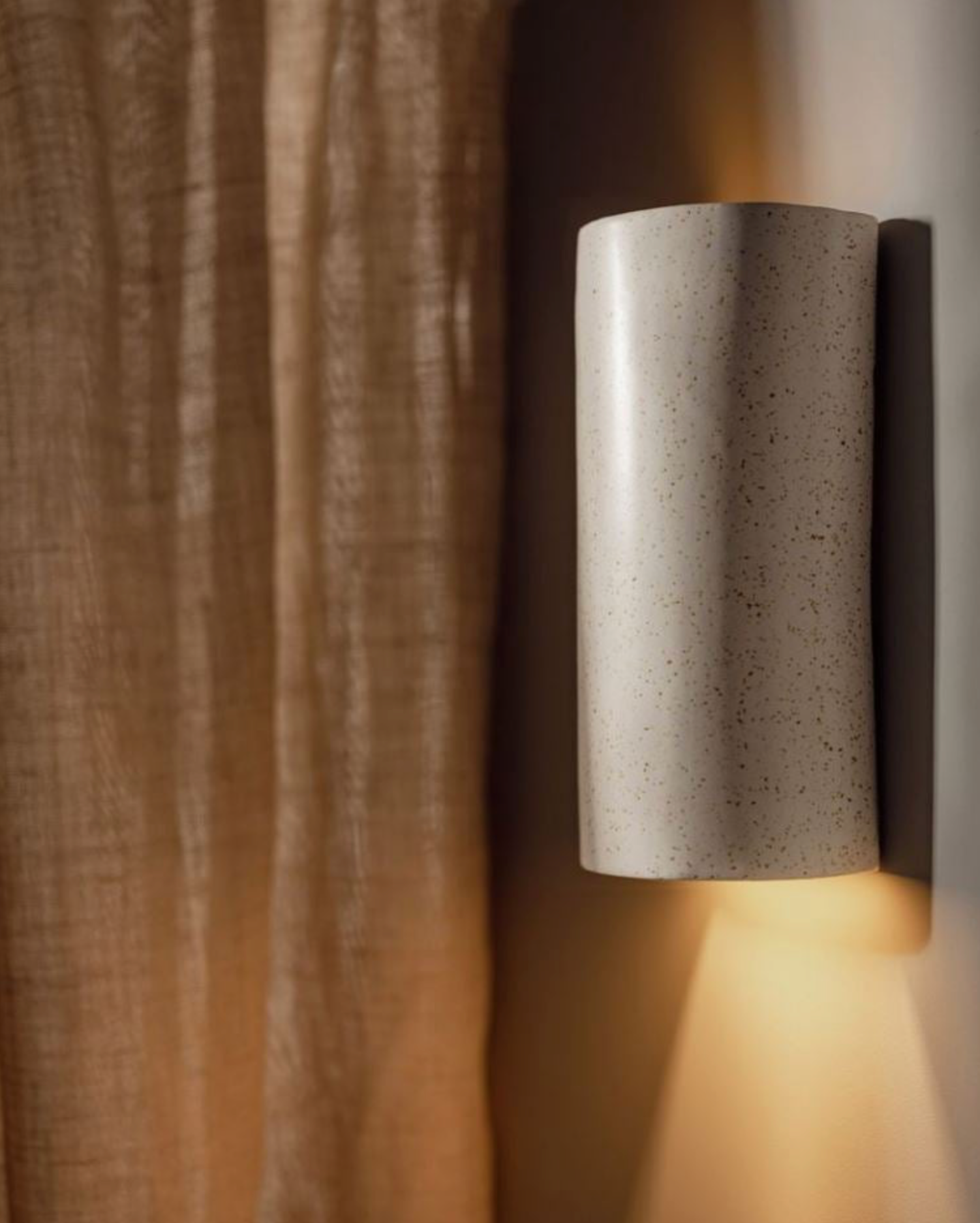 Cylindrical ceramic indoor wall light fixture on a textured wall.