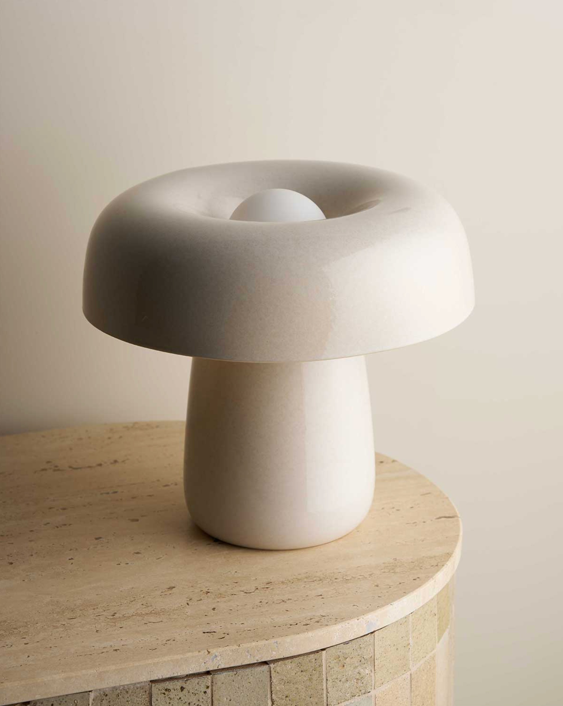 White mushroom-shaped ceramic lamp on a round stone surface with a neutral background