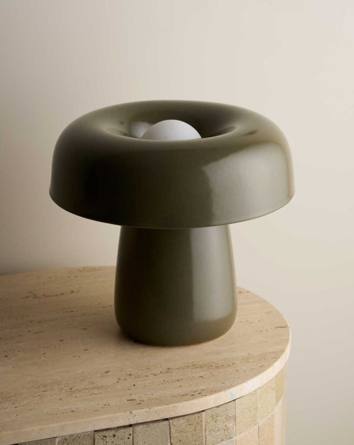 Modern olive green ceramic lamp on a wooden surface with a neutral background