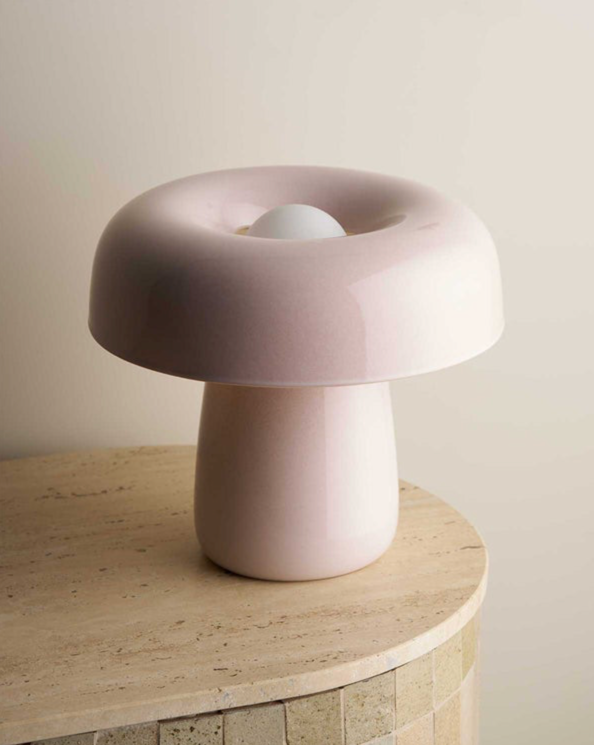 Pink mushroom-shaped ceramic lamp on a wooden surface with a neutral background