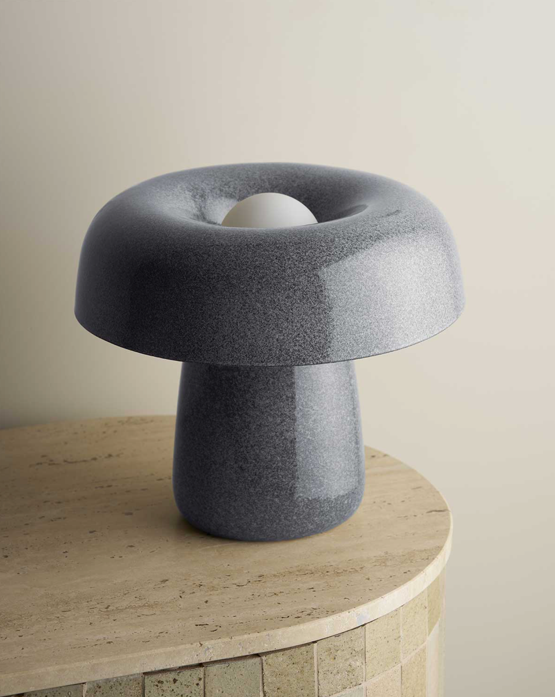 Grey table lamp on a stone pedestal against a beige wall