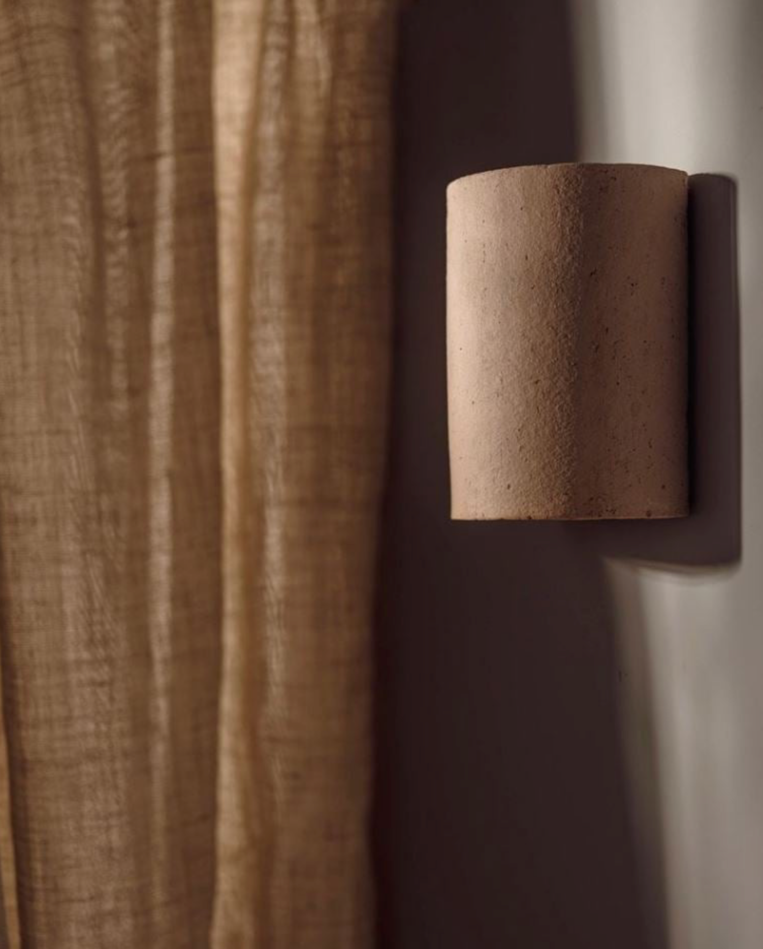 Textured wall sconce against a brown curtain