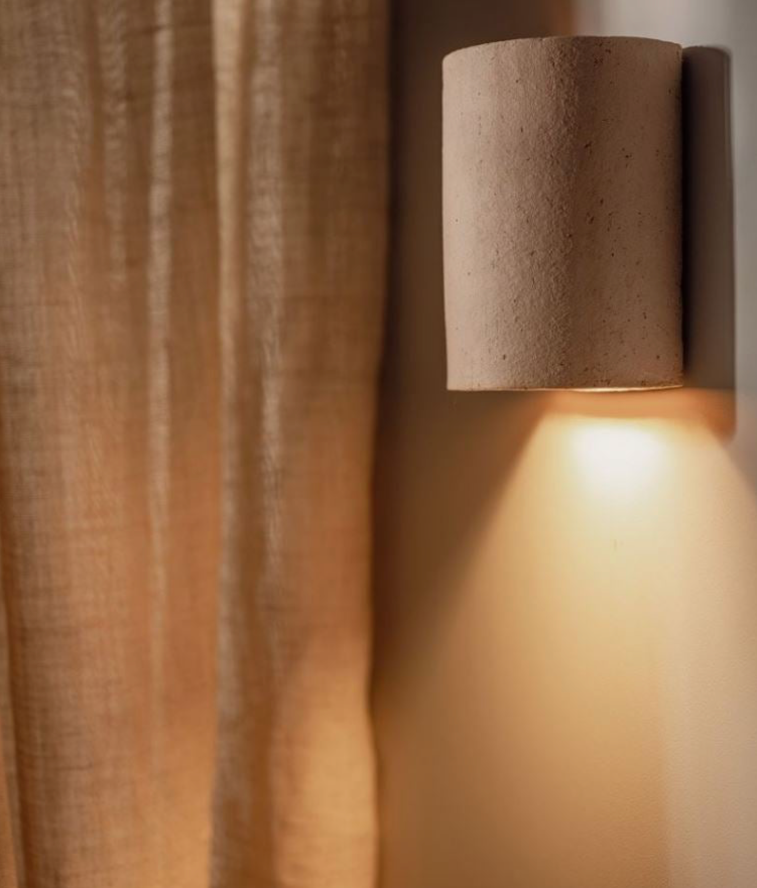 Cylindrical clay wall light fixture on a textured wall with soft glow