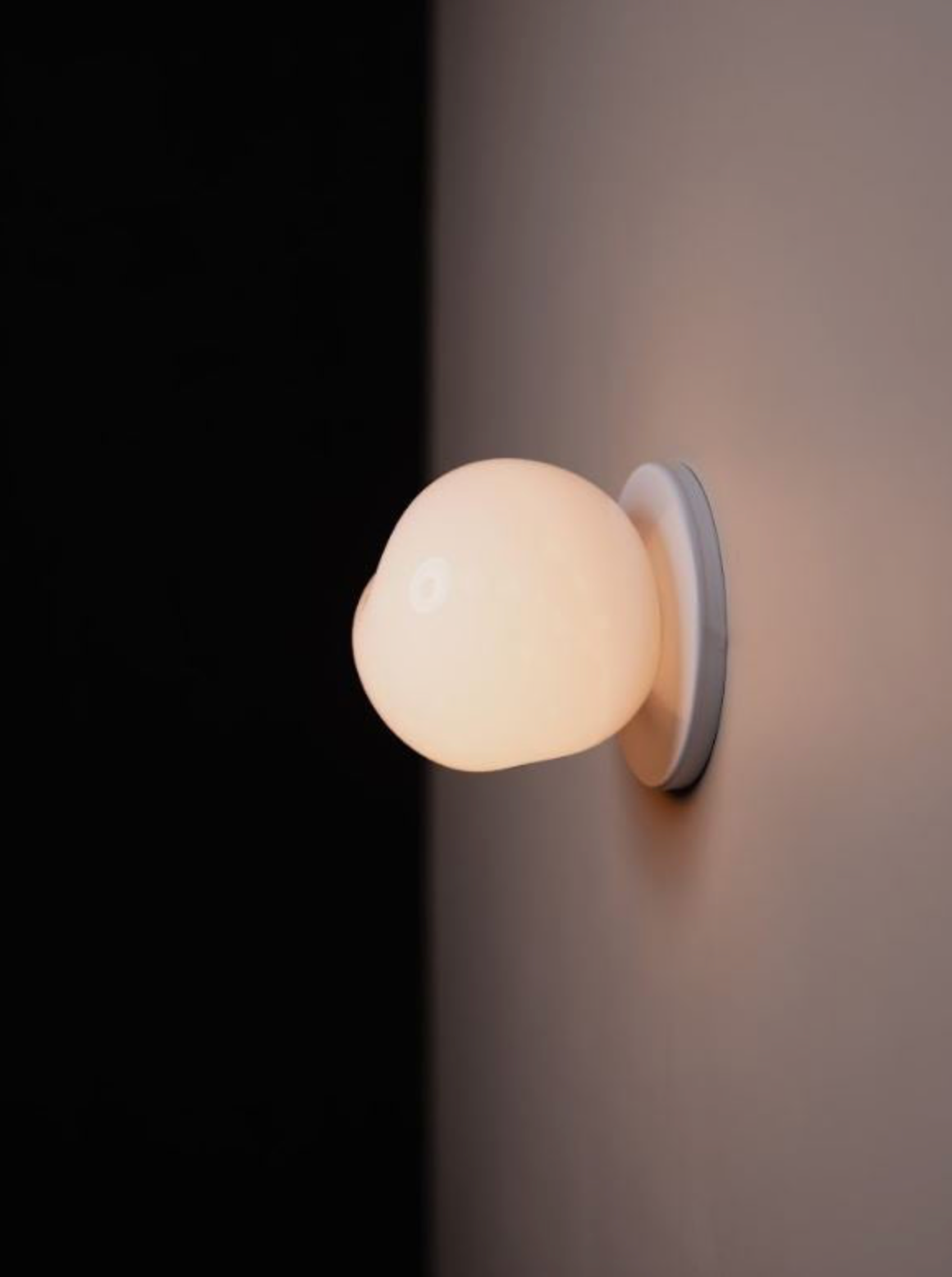 Wall-mounted light fixture with a spherical mouth blown glass shade on a dark background