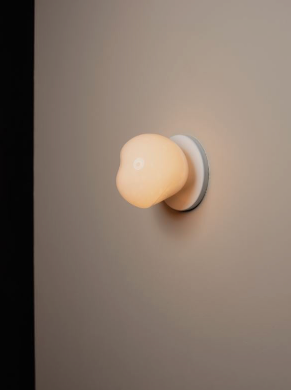 Wall-mounted light fixture with a round, beige lampshade on a neutral wall.