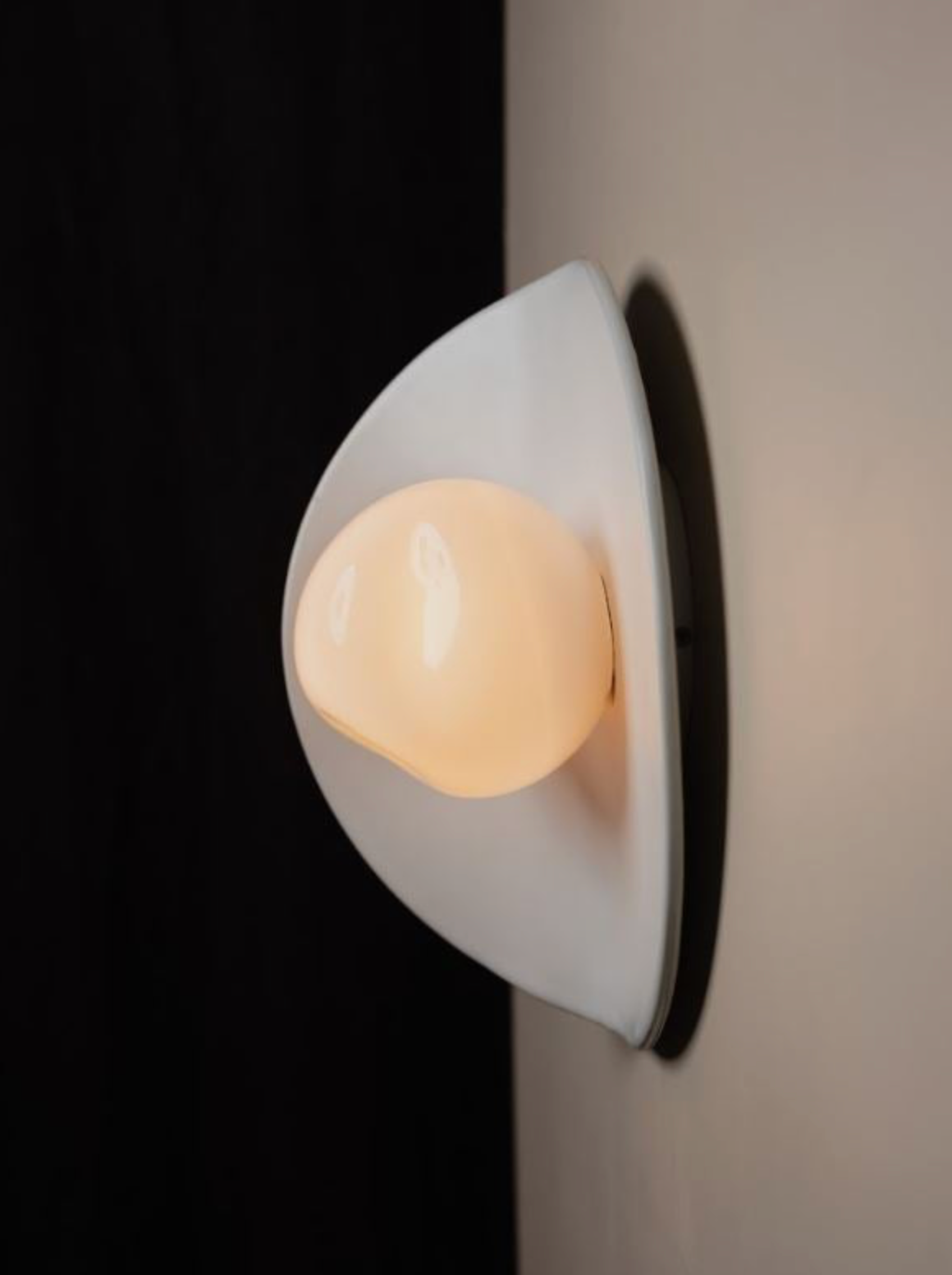 Wall-mounted light fixture with a white base and beige bulb on a neutral background