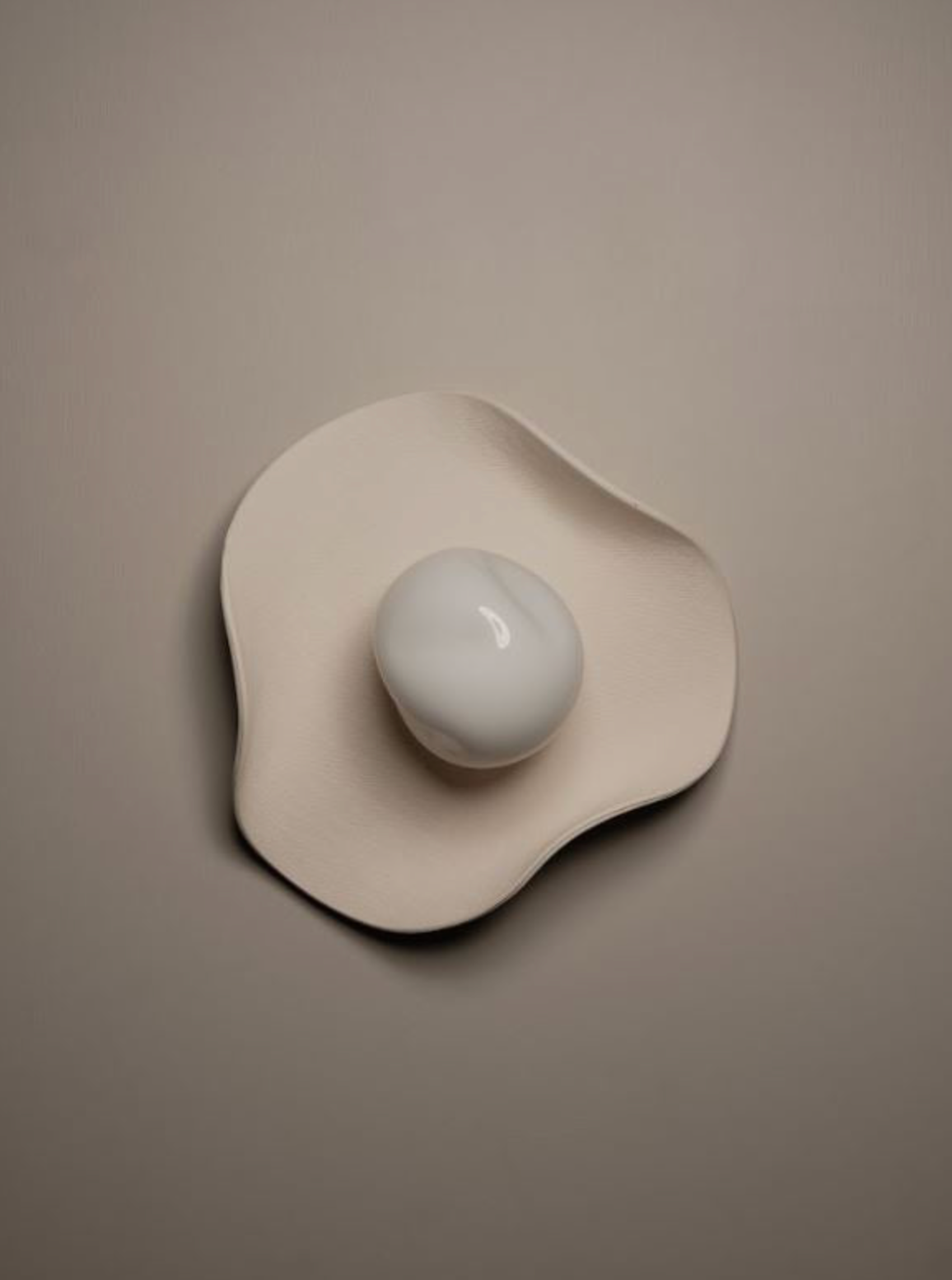 Ceramic wall art piece with a smooth, rounded design on a beige background