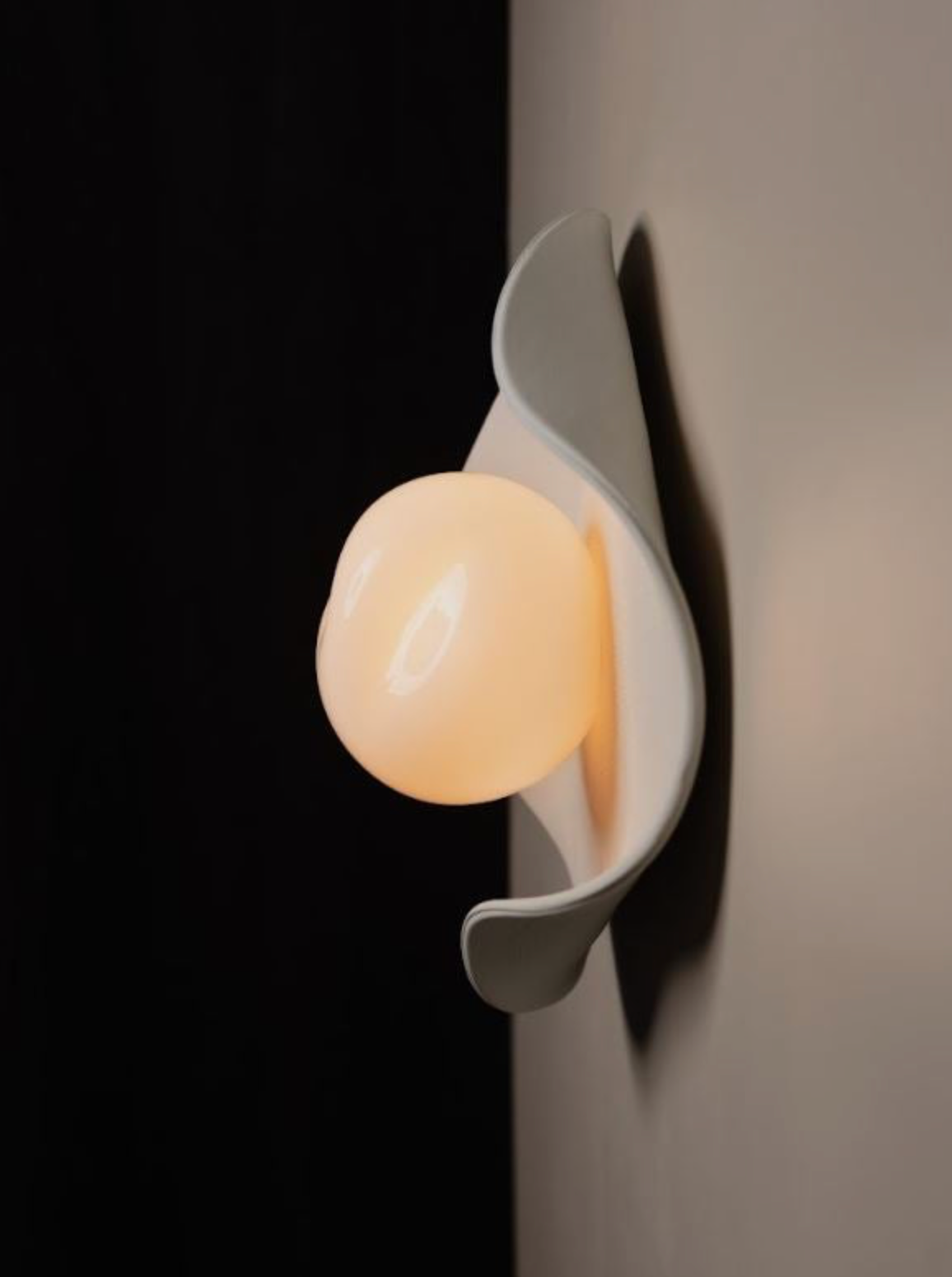 Close-up of a white wall sconce with a round object on a dark background