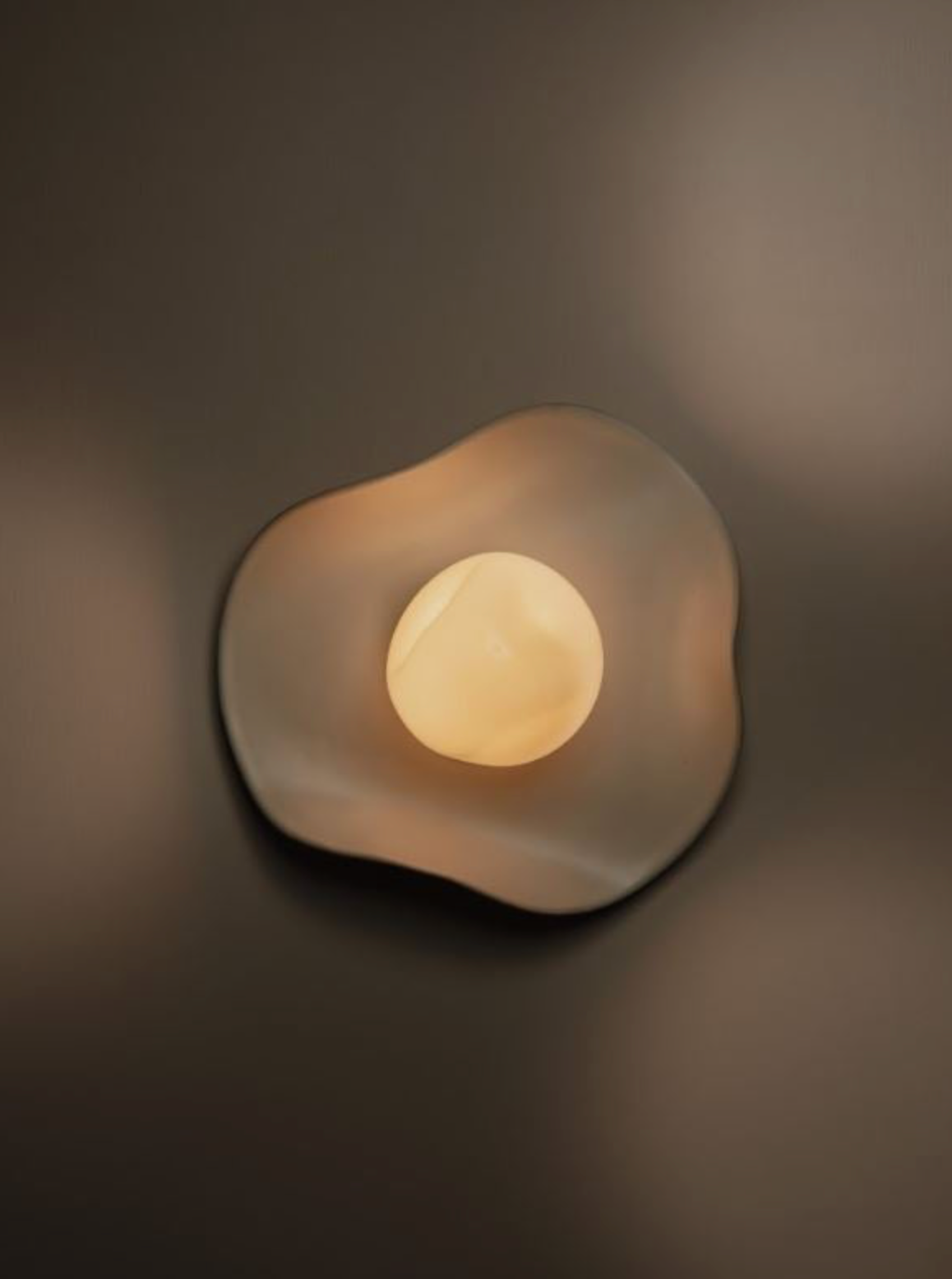 Cylindrical curved wall light fixture with a soft glow on a moody background