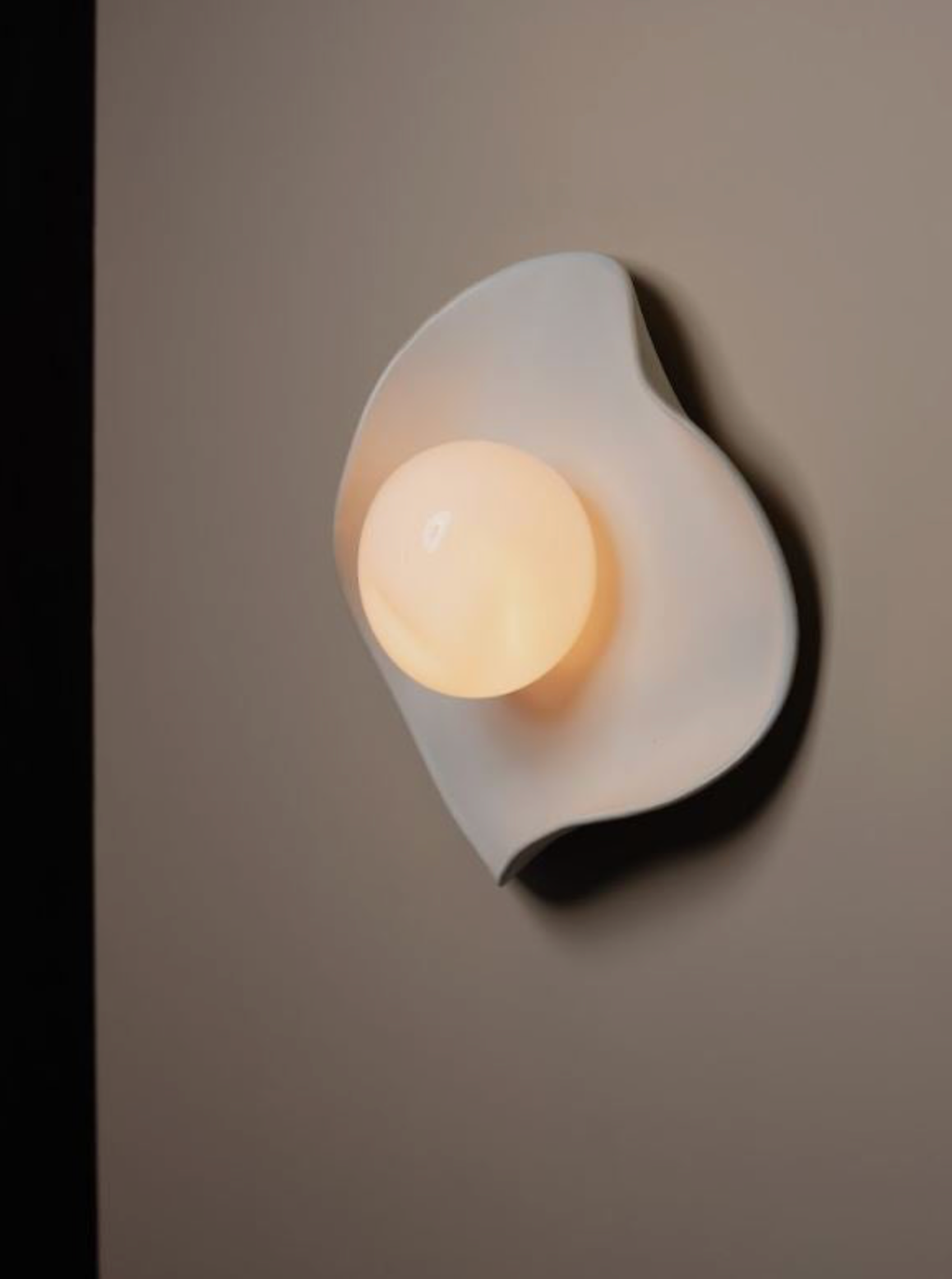 Wall-mounted light fixture with a round mouth blown glass bulb on a plain wall
