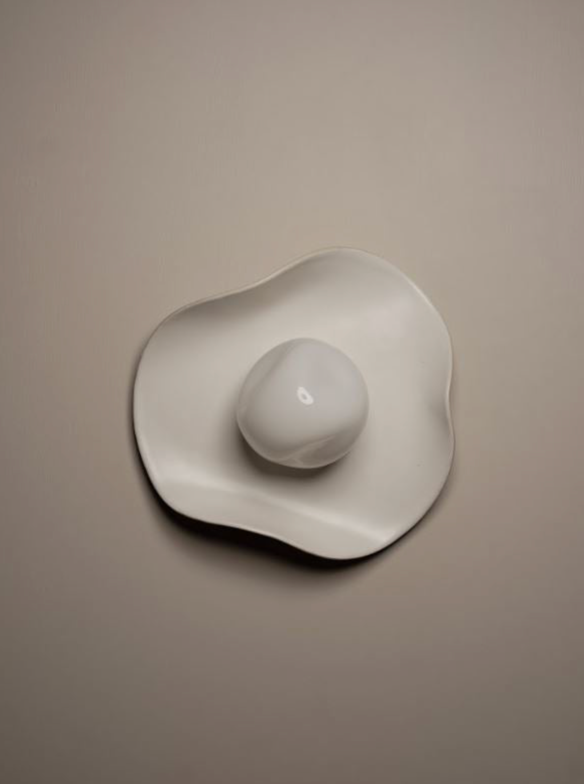 White hand made ceramic and glass wall sconce on a beige background