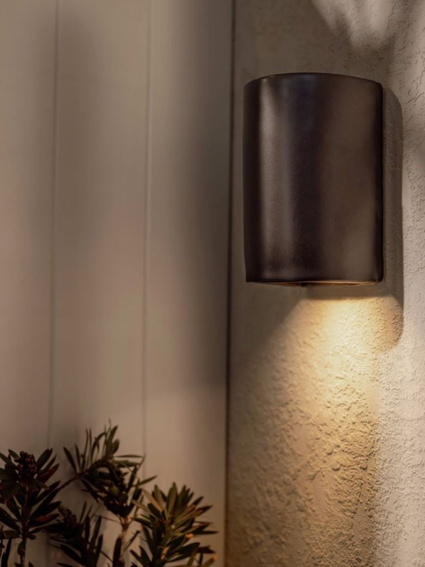 Dark outdoor wall light fixture on a textured wall with soft glow
