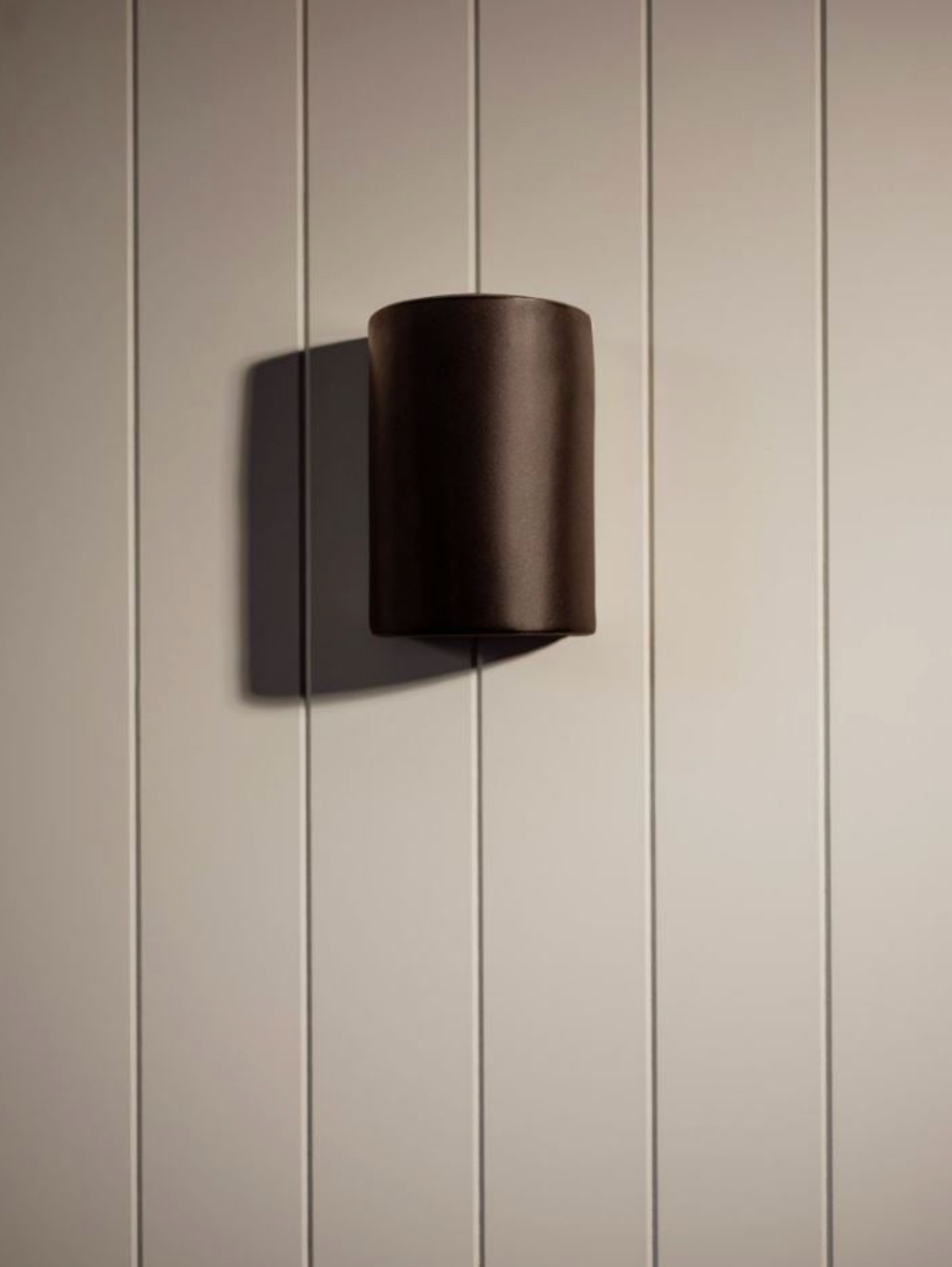 Black ceramic wall light fixture on a beige vj paneled wall