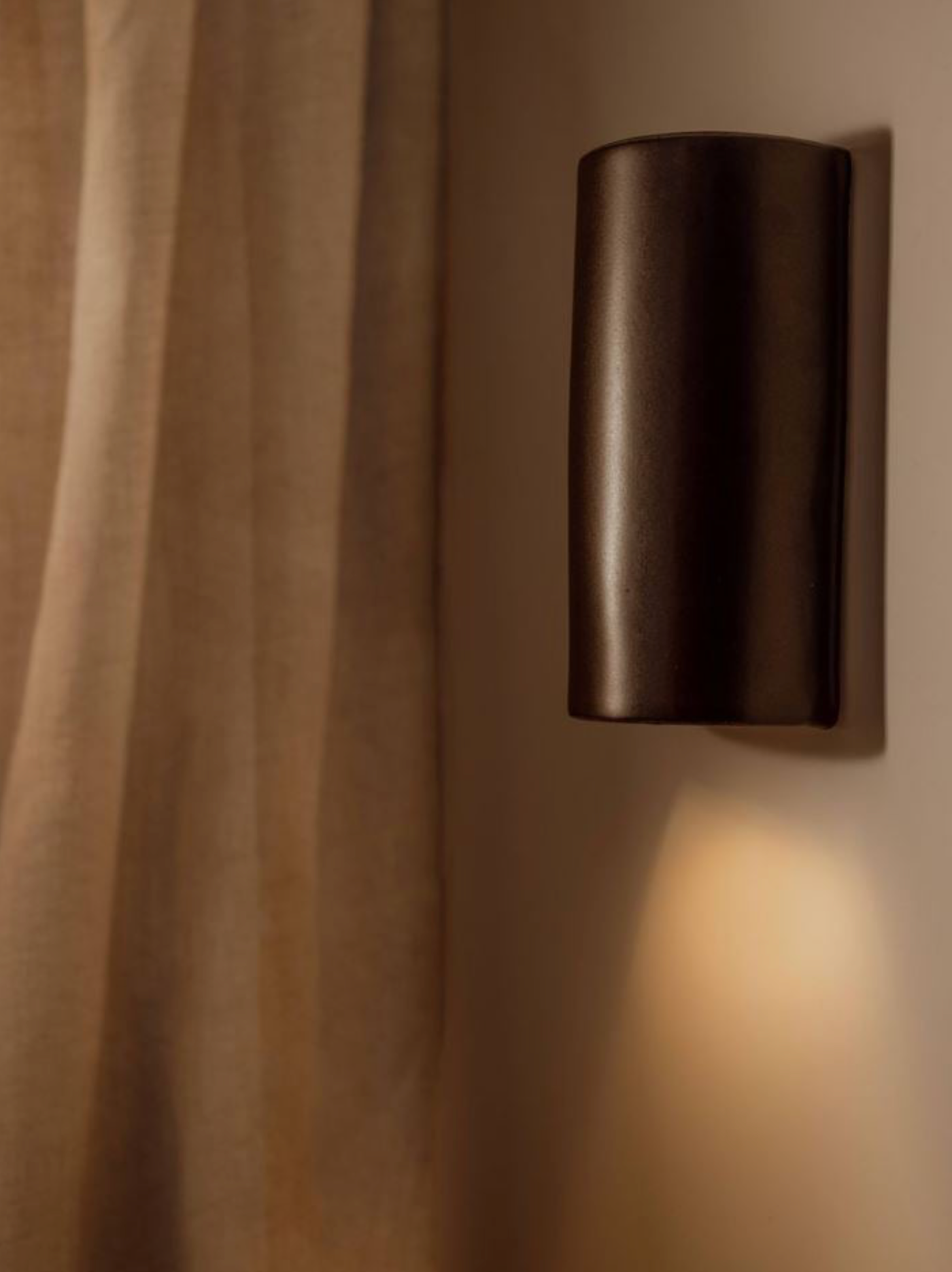 Dark cylindrical wall sconce on a beige wall with soft shadows