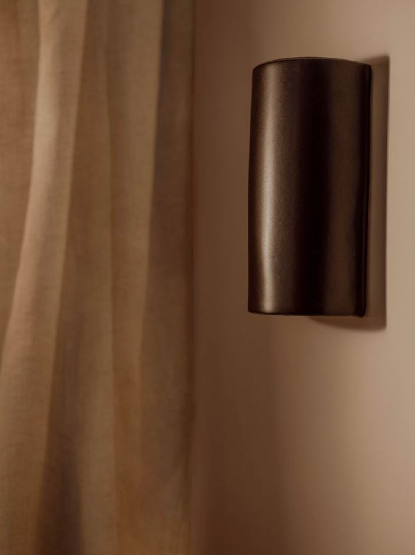 Modern hand made black cylindrical wall sconce on a beige wall. 