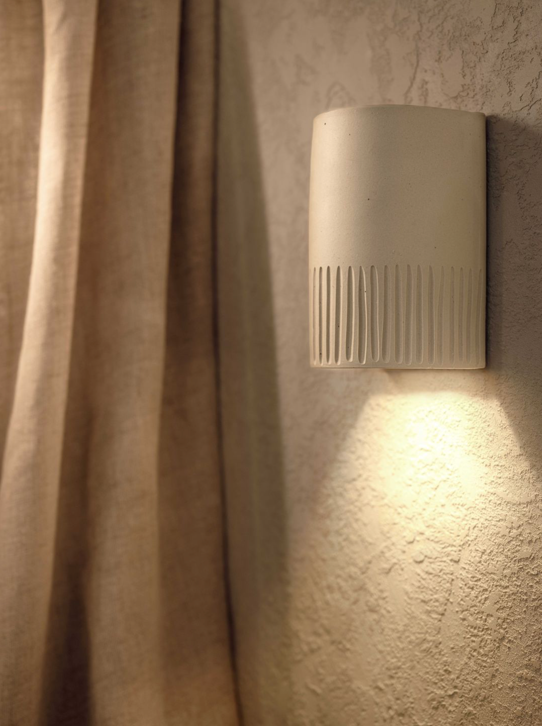 Wall-mounted light fixture on a textured wall with a curtain in the background
