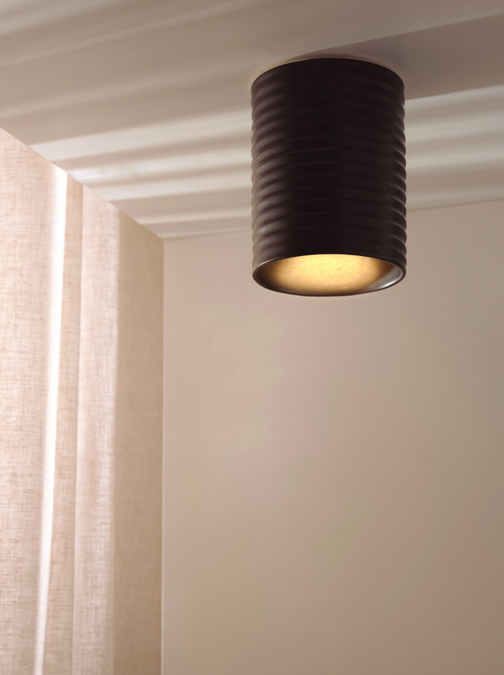 Black ceiling light fixture on a neutral wall with curtains in the background